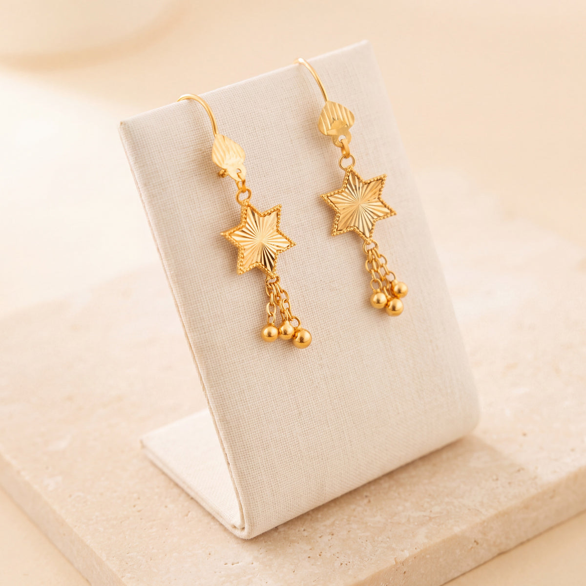 Star Earrings 1 – Gold star with chains, on travertine